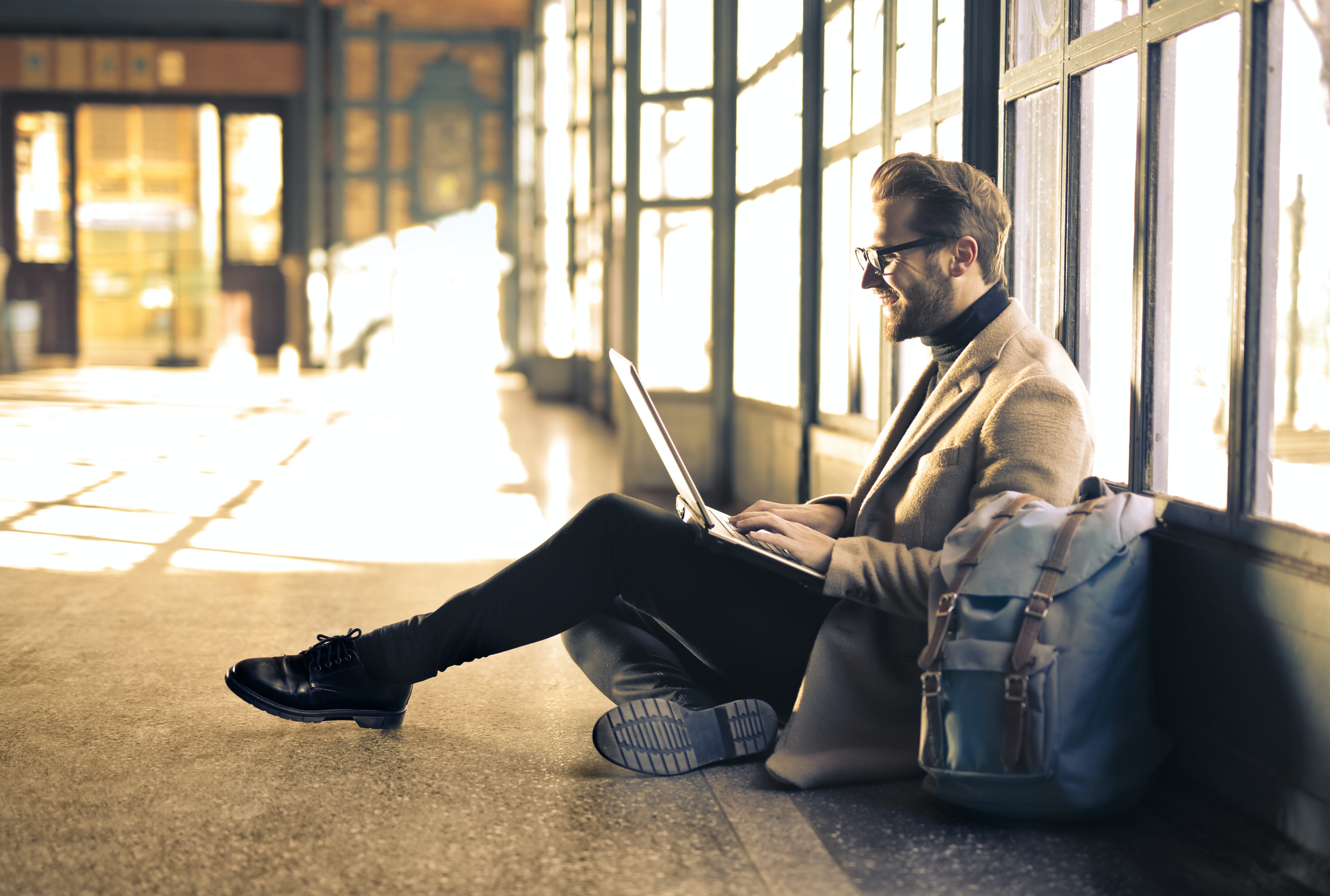 Person smiling at computer while sitting on the floor next to his backpack