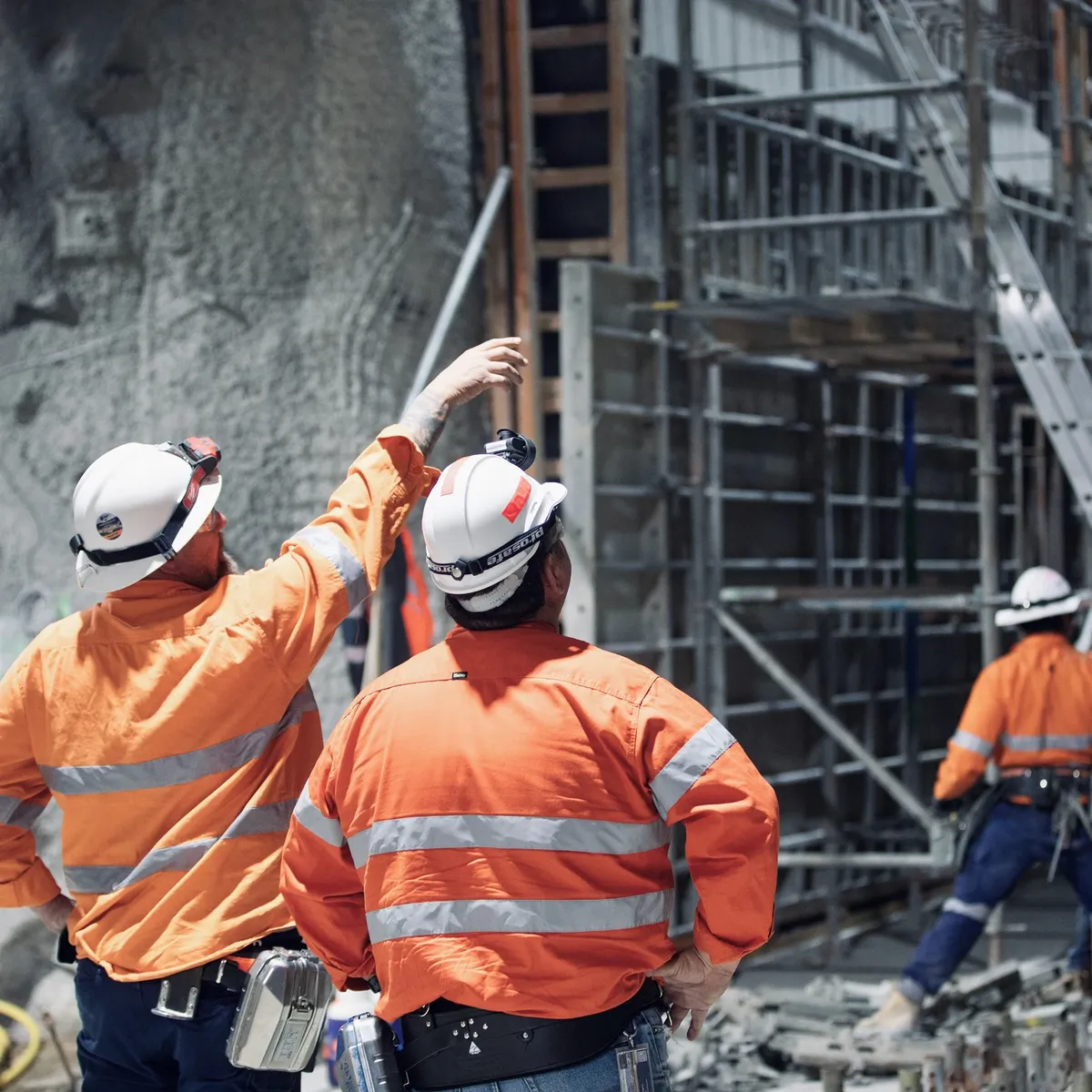 Two men in helmets and high-visibility jackets inspect construction progress