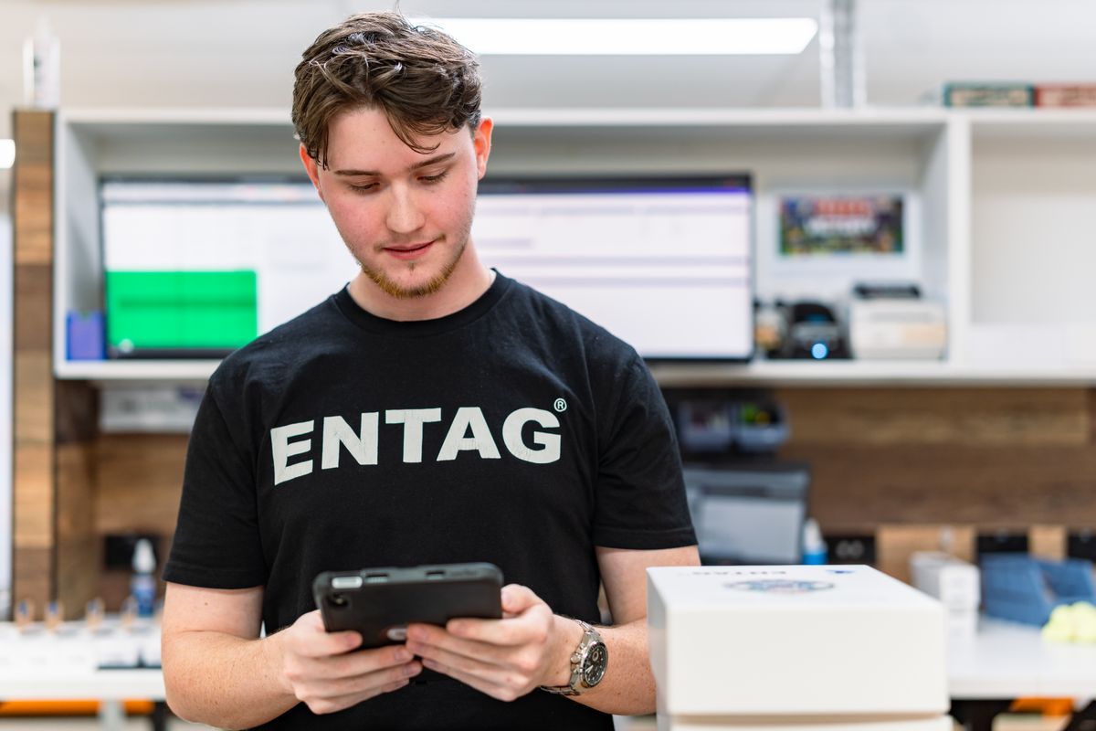 A young man wearing an ENTAG branded t-shirt is shown using a tablet.