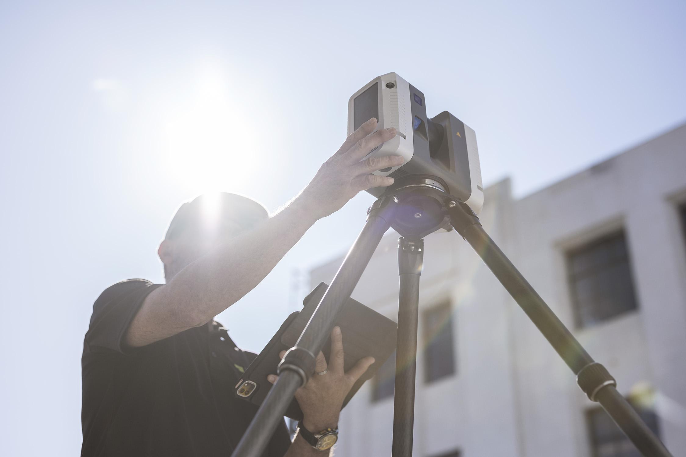 A man operating a tripod-mounted Trimble SX10 scanner, used by the HG Survey Team to capture 3D scans in 2023.