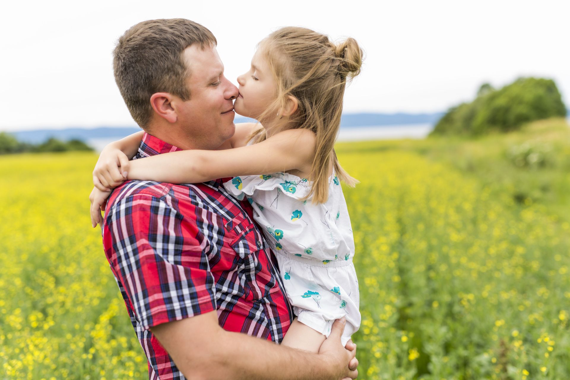 A father holding his young daughter in a yellow flower field, sharing a kiss on the nose. The joyful scene highlights love, family, and connection with nature — perfect for an eco-friendly Father’s Day theme.