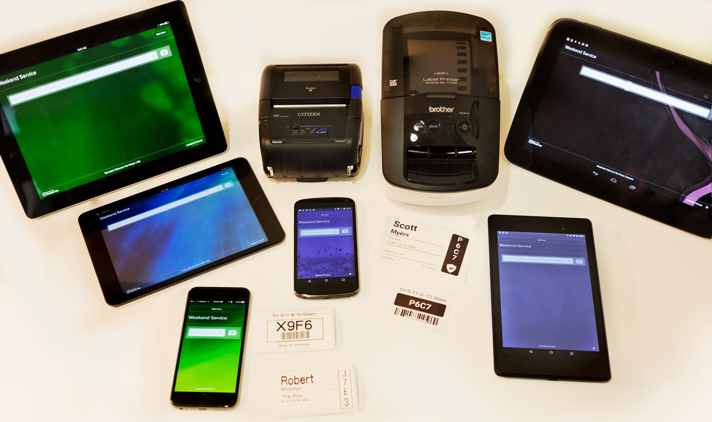Two label printers on a table with two phones and four tablets of different sizes.