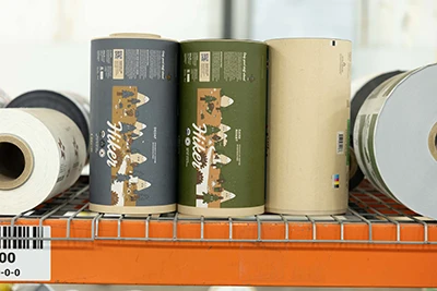 Several custom-printed roll stock on an orange metal shelf, featuring designs and barcodes.