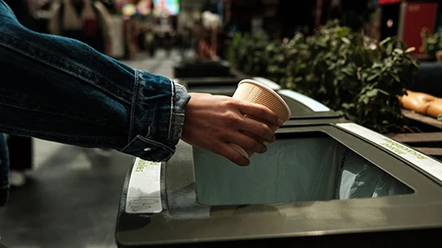 Person throwing paper cup in recycling bin