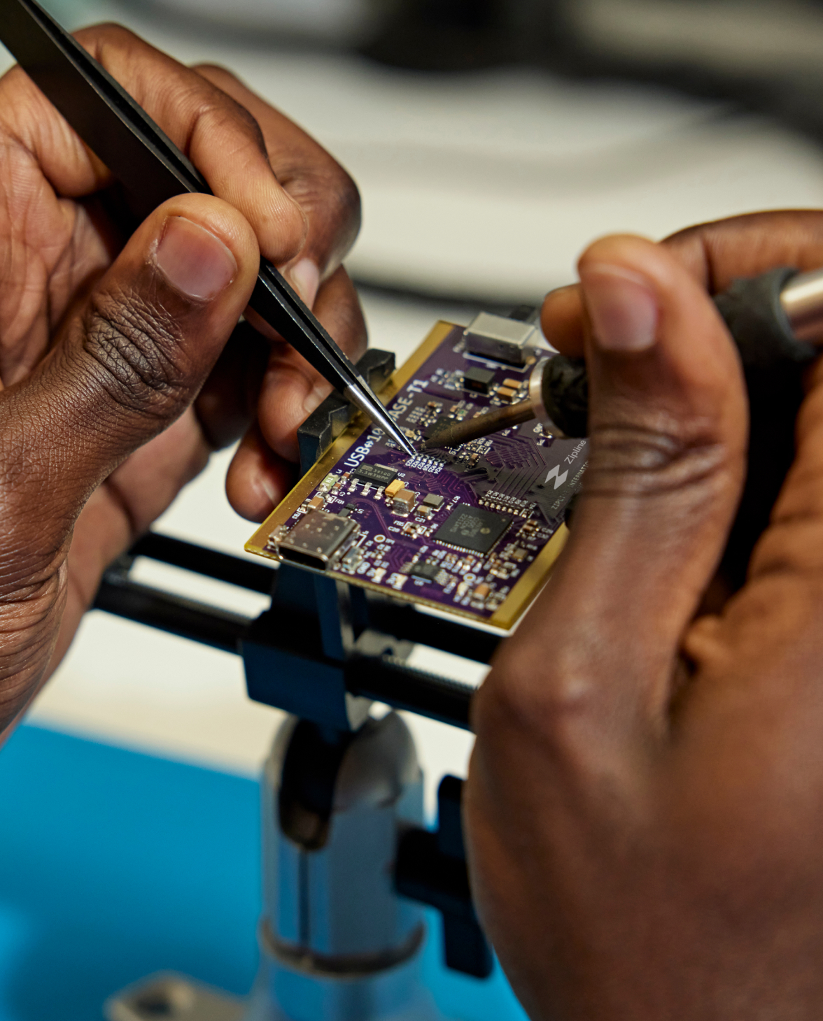 Hands of a black man holding tweezers while working on a printed circuit board