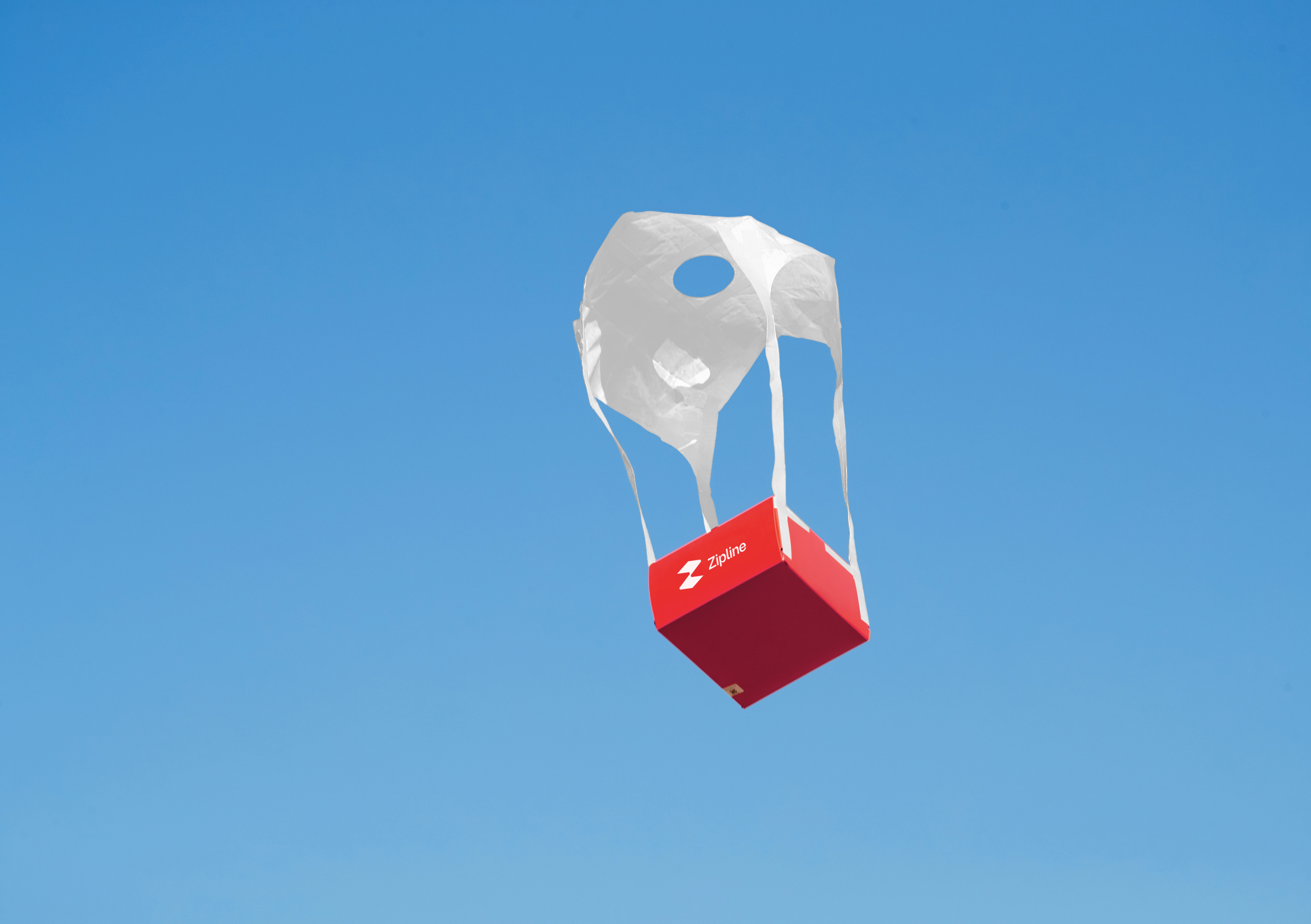 Zipline delivery package descending under its precision delivery system against a blue sky