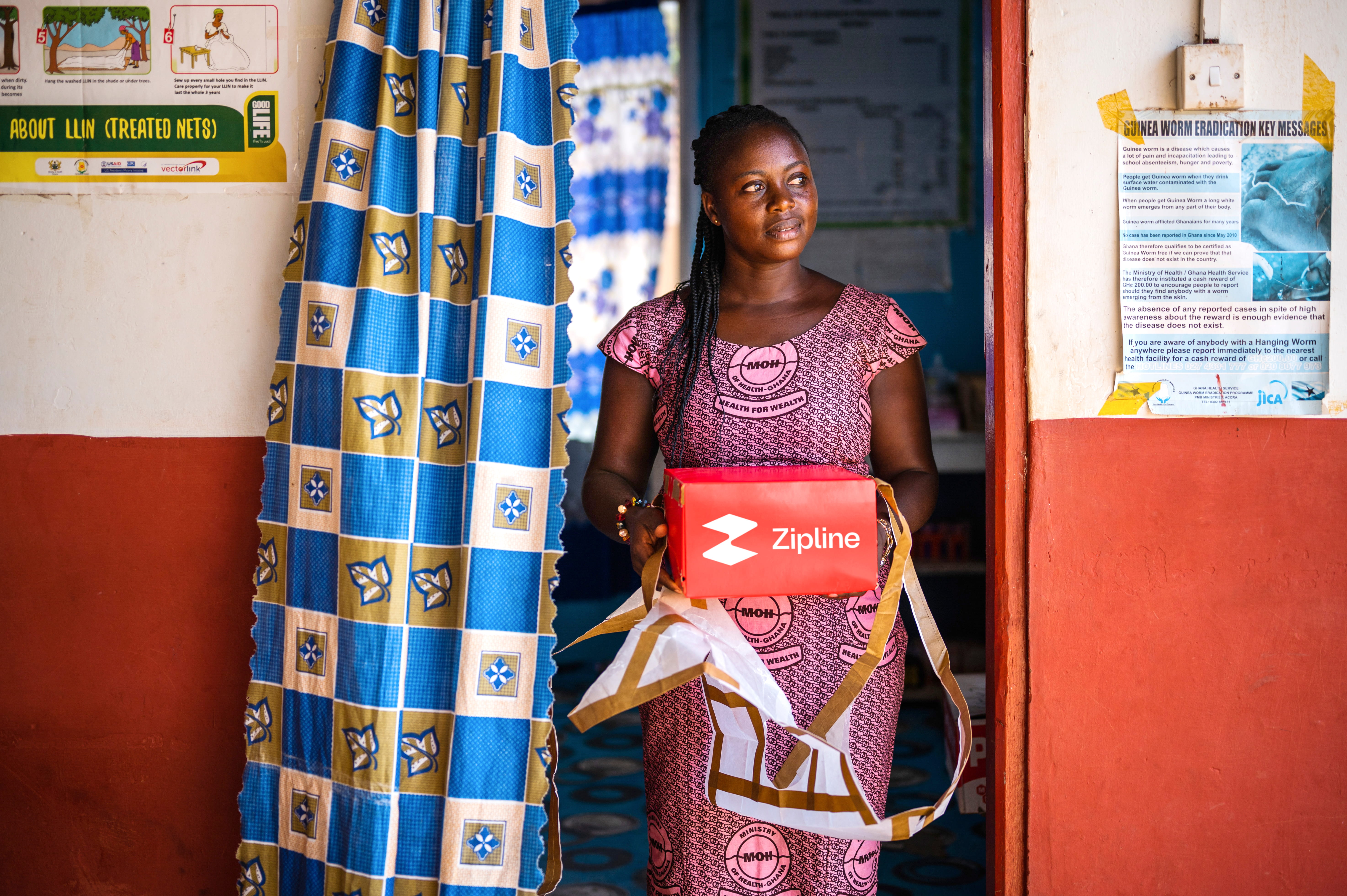 African woman stands in doorway holding Zipline delivery package