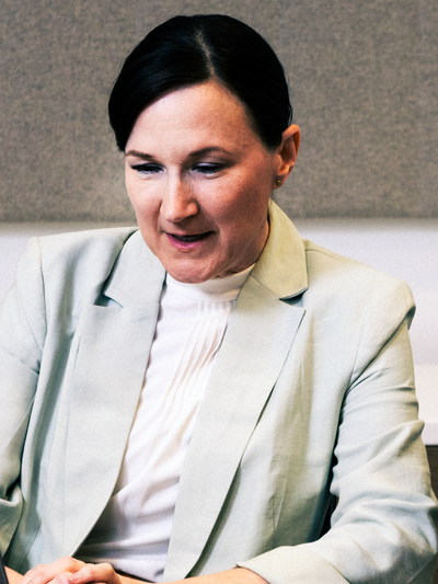 A hospital administrator wearing a grey suit jacket and white shirt sitting at a table. Eyes pointed down with a pleased look on her face.