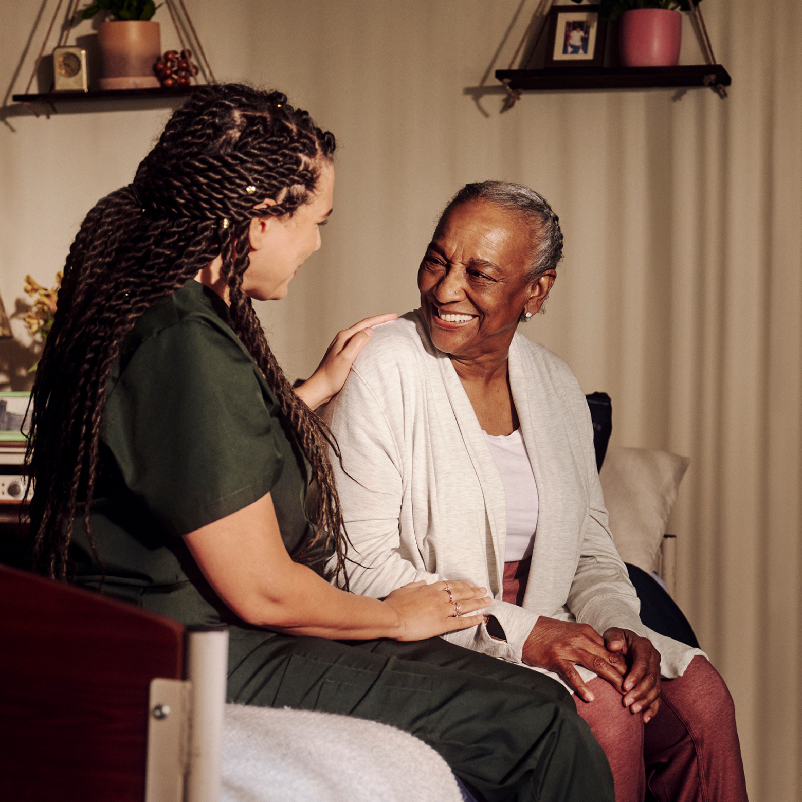 An independent professional wearing dark green scrubs places her hand on a smiling resident's shoulder.