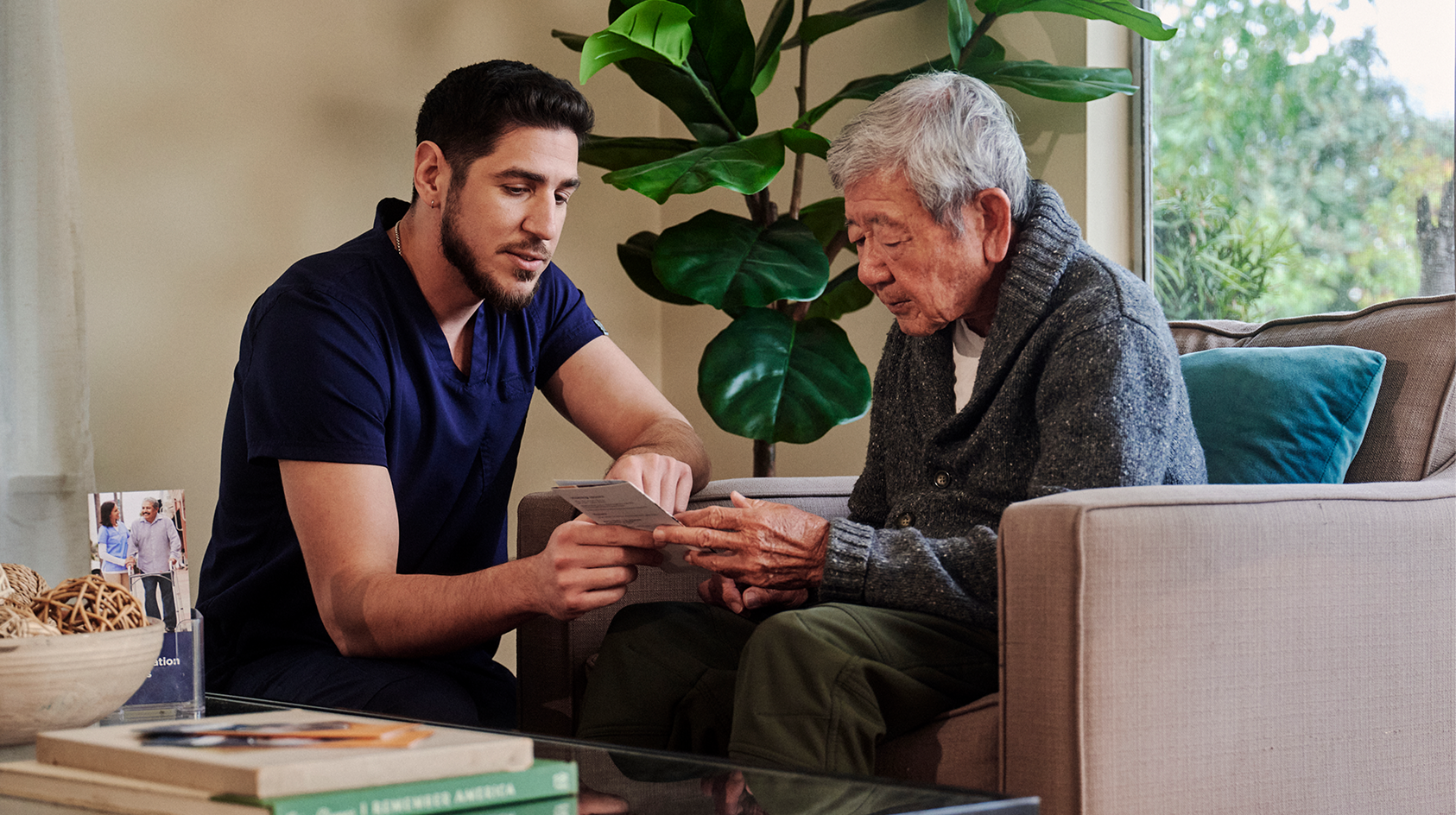 A young independent professional in navy scrubs shows something to a male resident wearing a grey sweater