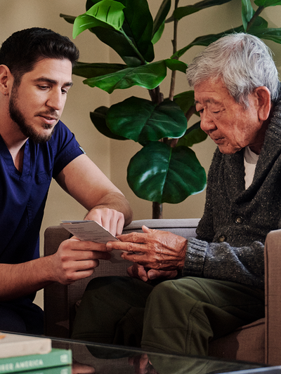 A young independent professional in navy scrubs shows something to a male resident wearing a grey sweater