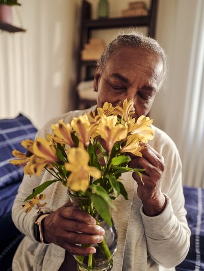 A woman in a skilled nursing facility smells a bouquet of yellow alstroemeria flowers