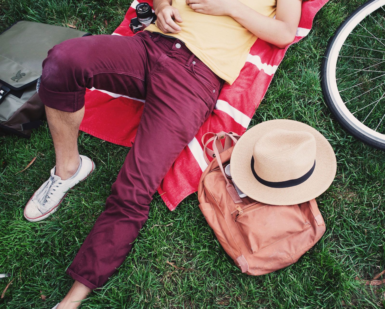 A cyclist relaxes at the park with their bags, hat, and bike resting next to them.