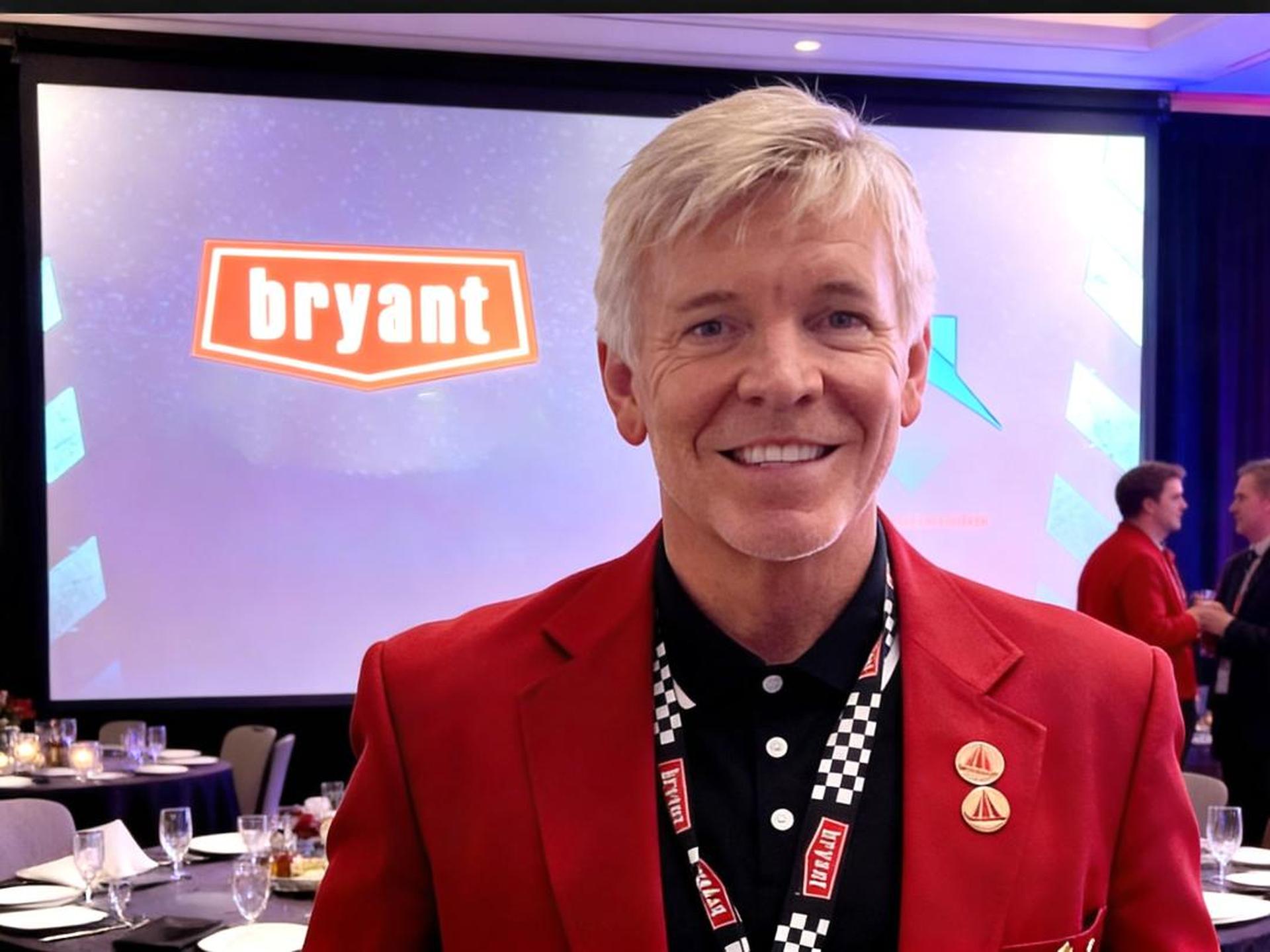 Matt Montgomery in a red blazer in front of the Bryant logo