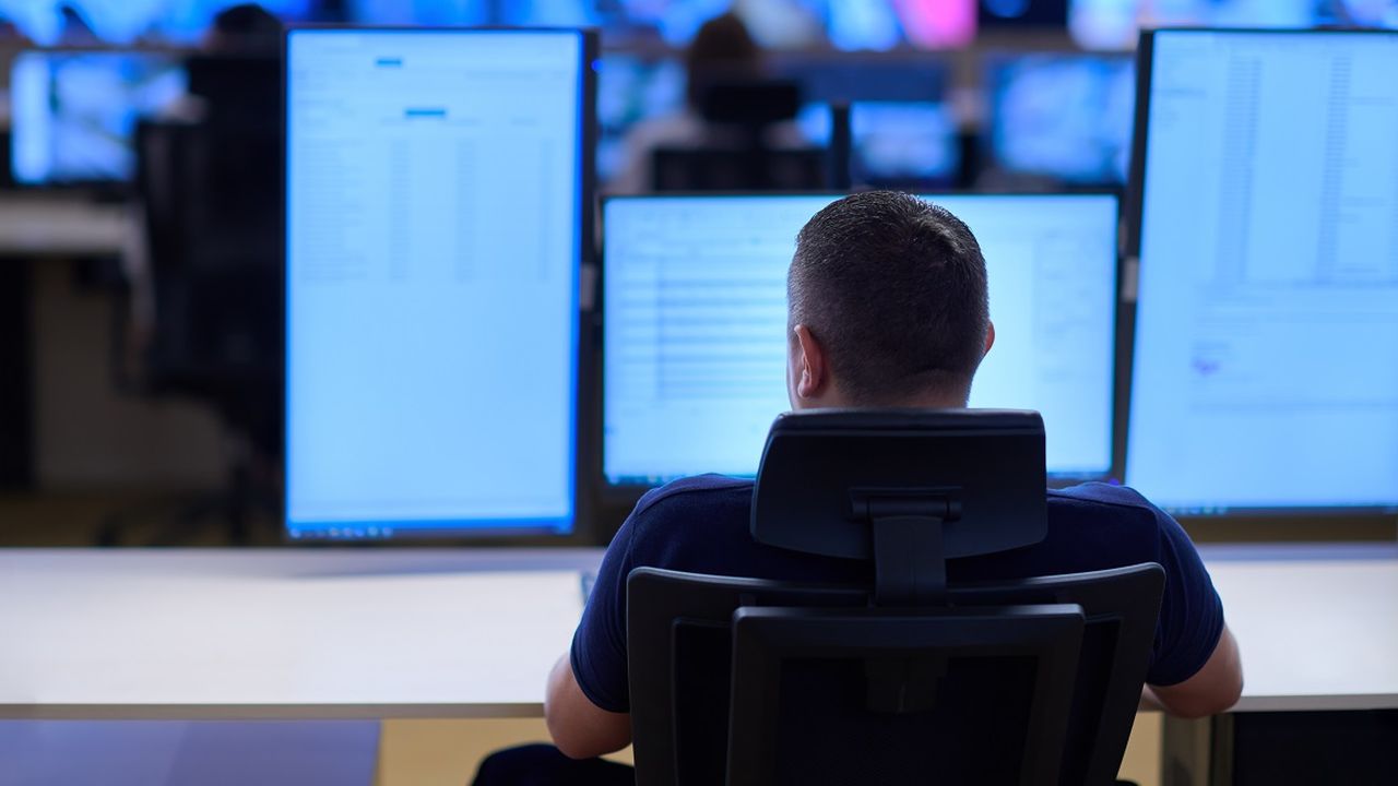 A man sitting on a desk in front of some computer screens