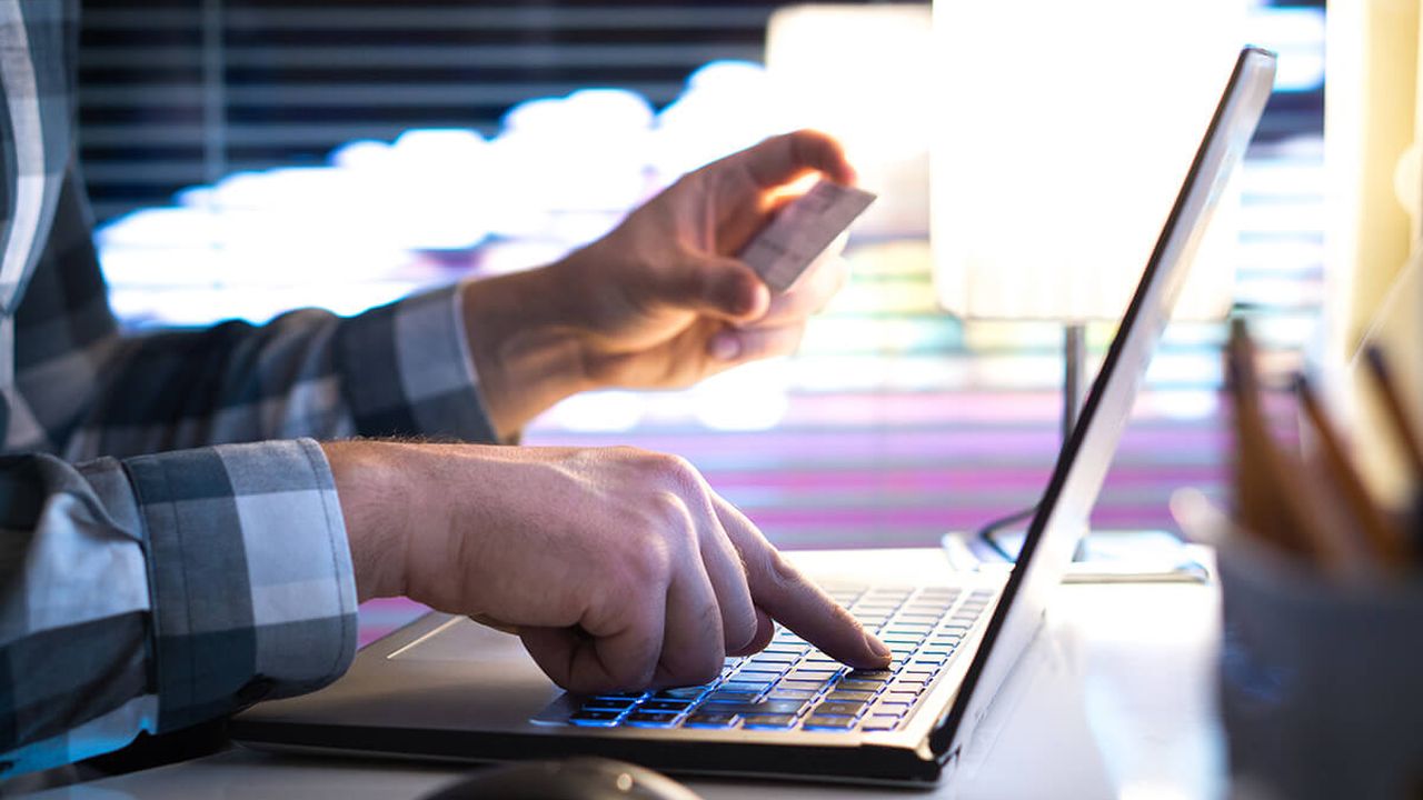 Stock photo of a person typing numbers on a laptop, while holding a credit card in their other hand