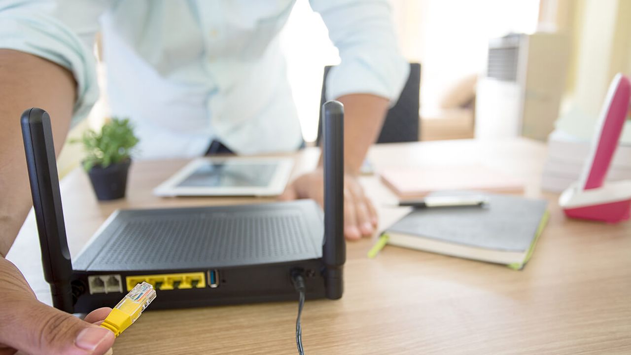 Photo of an internet router with a person reaching behind it with a network cable
