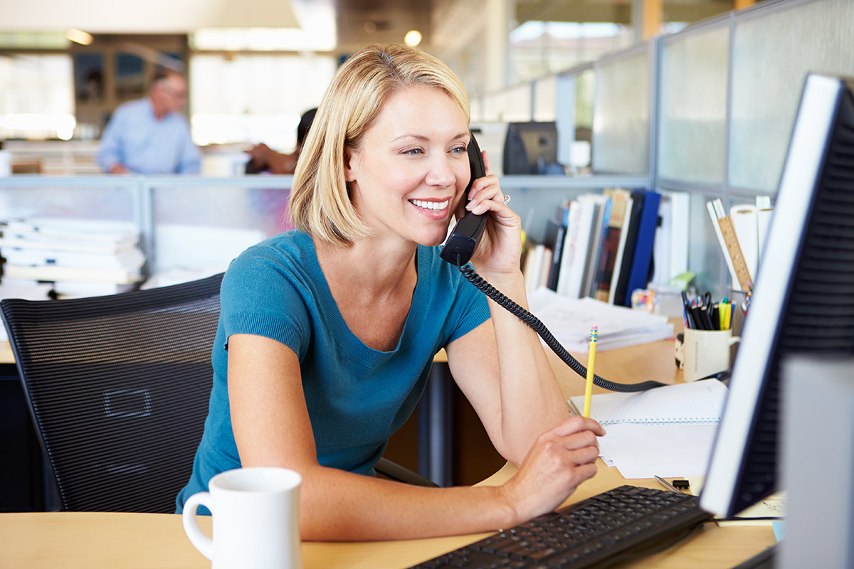 A woman on the phone while on a computer in an office 