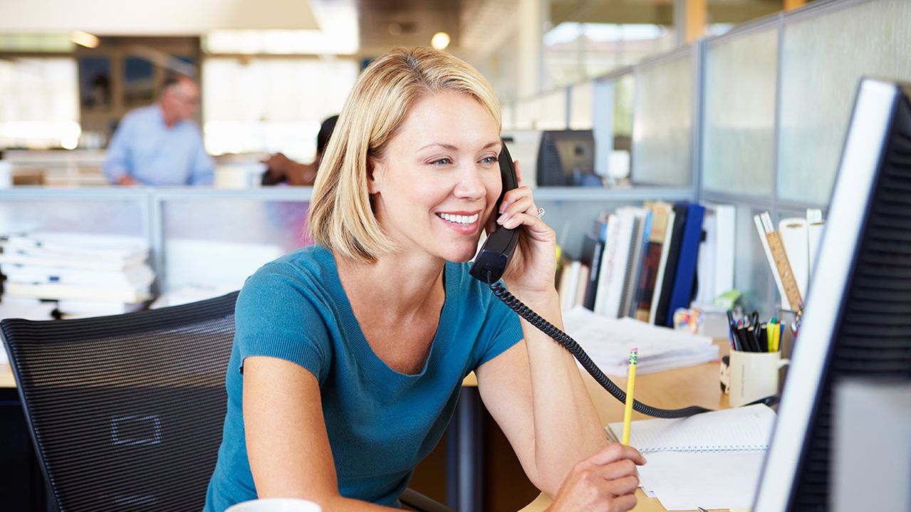 A woman on the phone while on a computer in an office