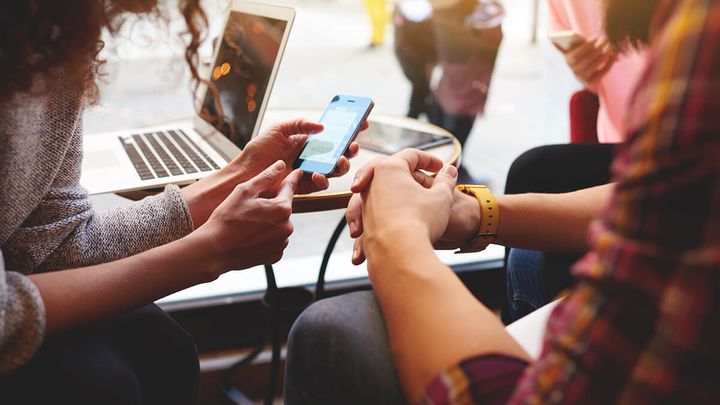 Photo of a person gesturing to a smartphone with another person
