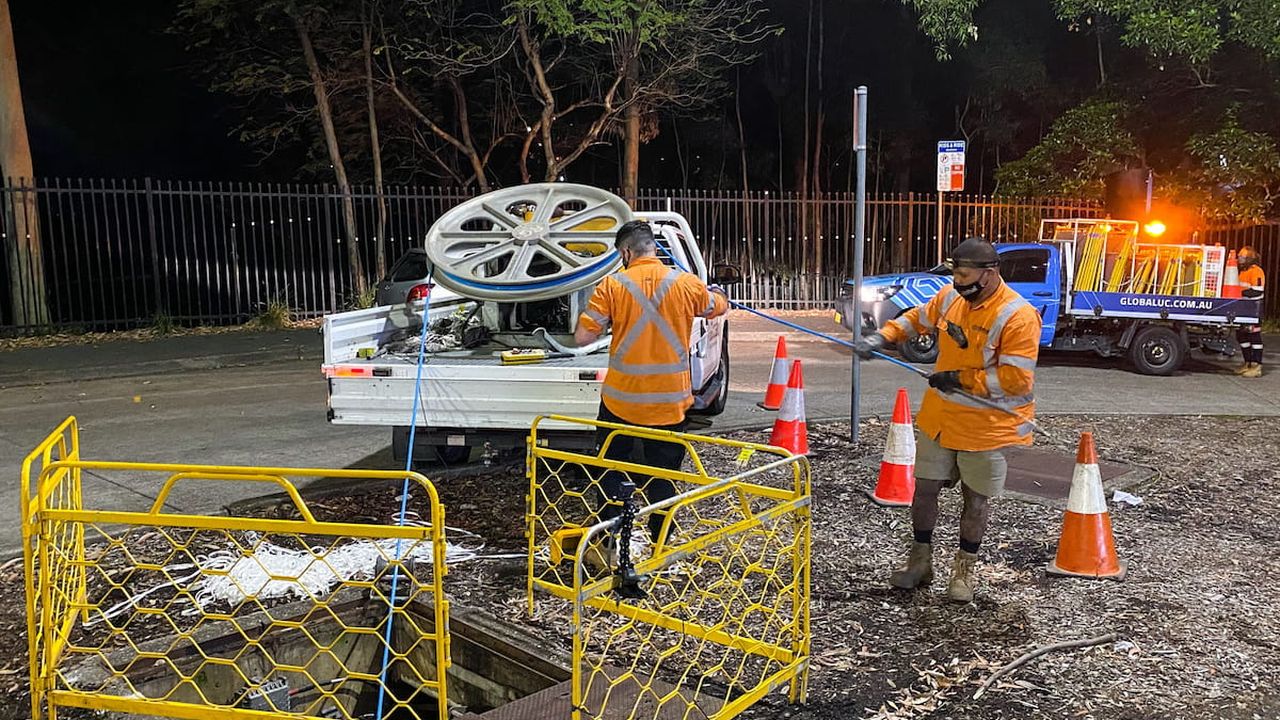 Two men dressed in orange reflective gear installing NBN fibre