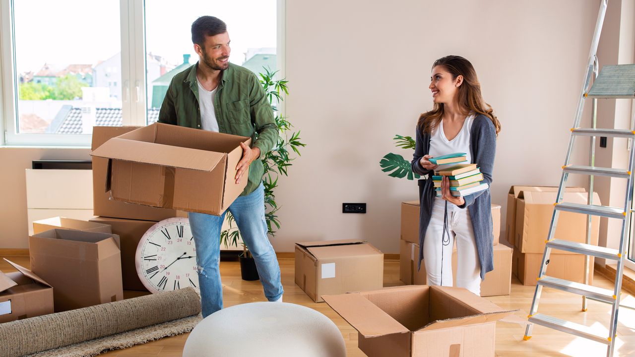 A couple moving house, with a man holding an empty box while the woman packs some books