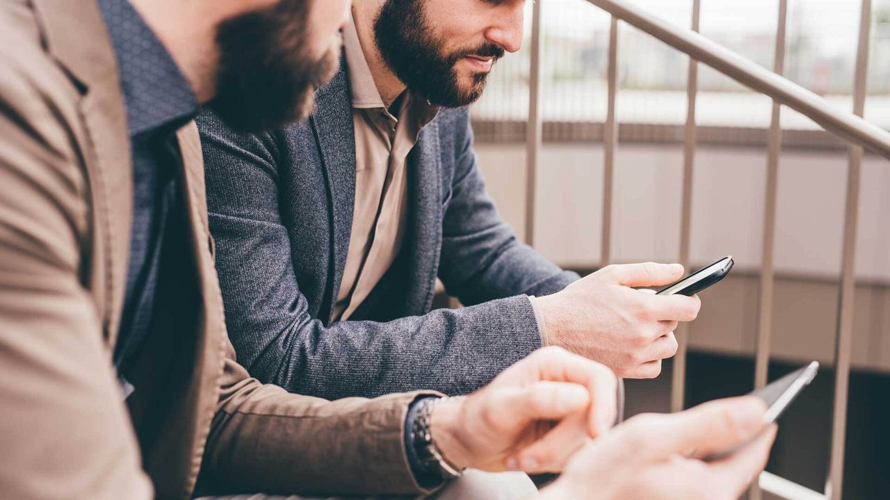Two businessmen looking at their respective smartphones