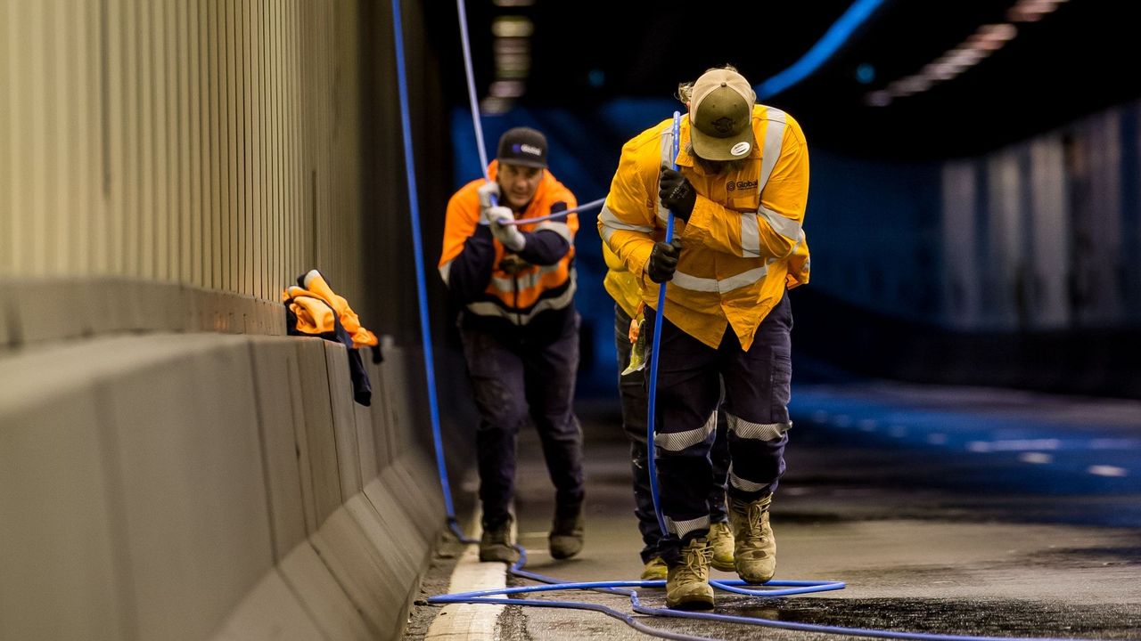 Two workers pull on fibre cable in tunnel