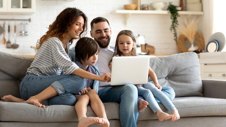 A man, woman, boy, and girl sitting on a couch looking at a laptop