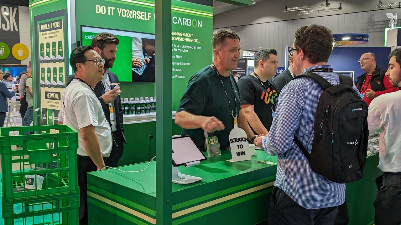 Aussie Broadband's Cisco Live 2023 booth: A trade show booth resembling a convenience store. The front banner says "Aussie Broadband convenience store" and there is a small, flag-like banner above that says "checkout". There are six Aussie Broadband staff members behind the counter, and three event attendees in front of the counter.