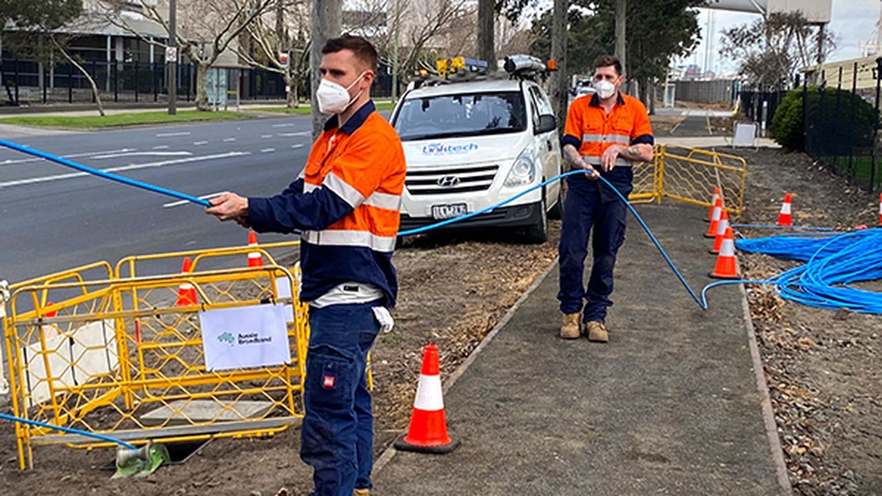 Two workers pull on fibre cable on footpath