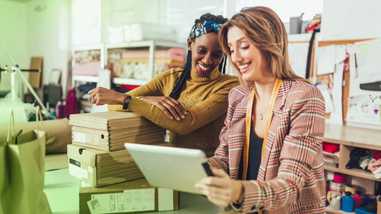 Two women in an office looking at a tablet one of the women is holding. Both women are smiling.