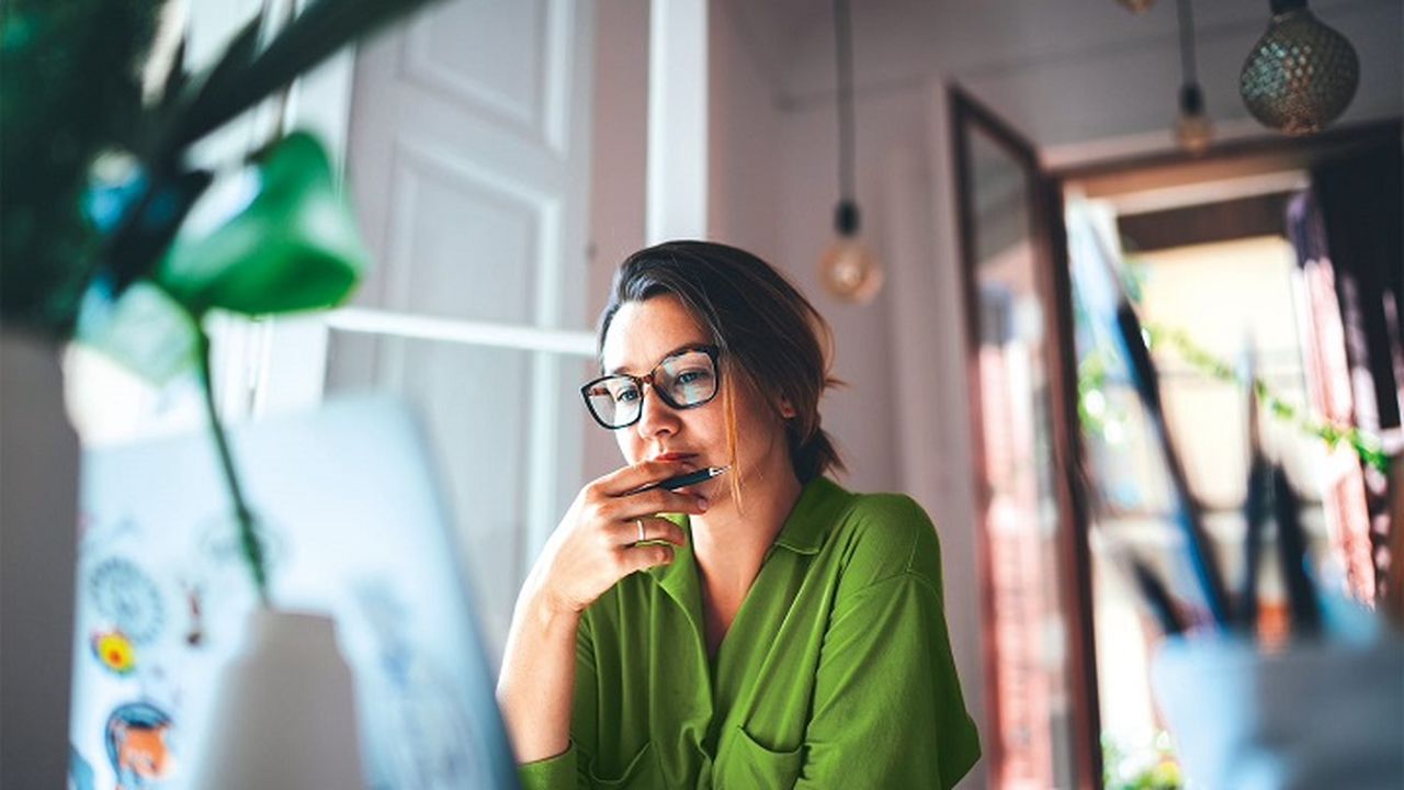 A woman sitting at a desk looking at a laptop.
