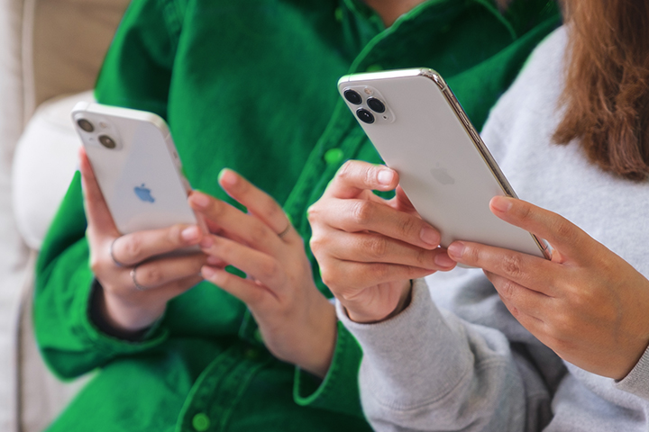 two people with their faces out of frame each holding a mobile phone with both hands.