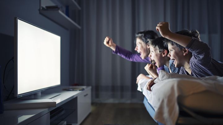 A photo of 3 family members watching TV excitedly