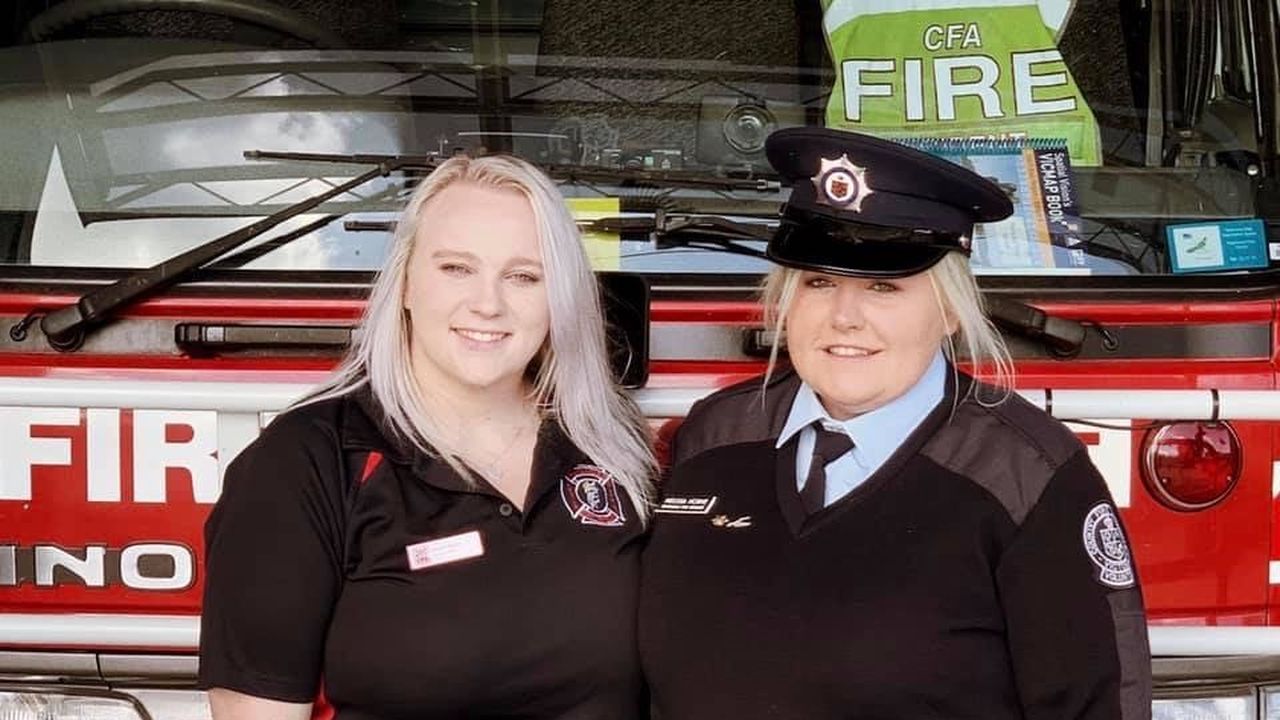 Two volunteer firefighters stand in front of red fire truck