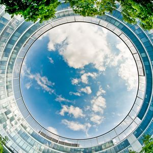 A circular image looking up at a sky with light clouds with buildings and trees around