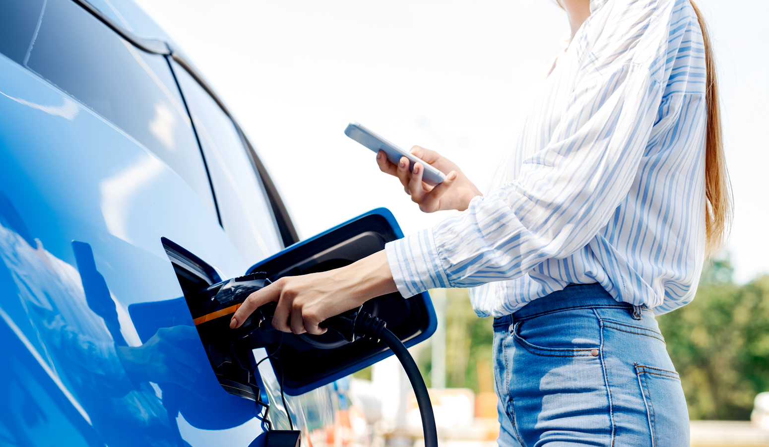 A woman charging her blue EV outside.