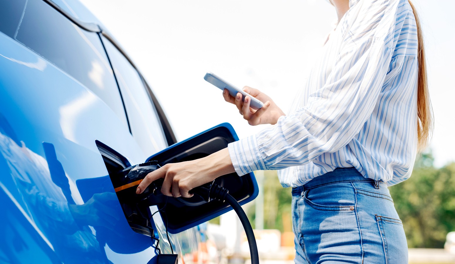 A woman charging her blue EV outside.