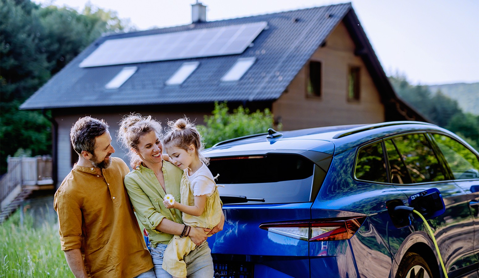 A couple and a young girl standing outside their house with solar panels and an electric vehicle.