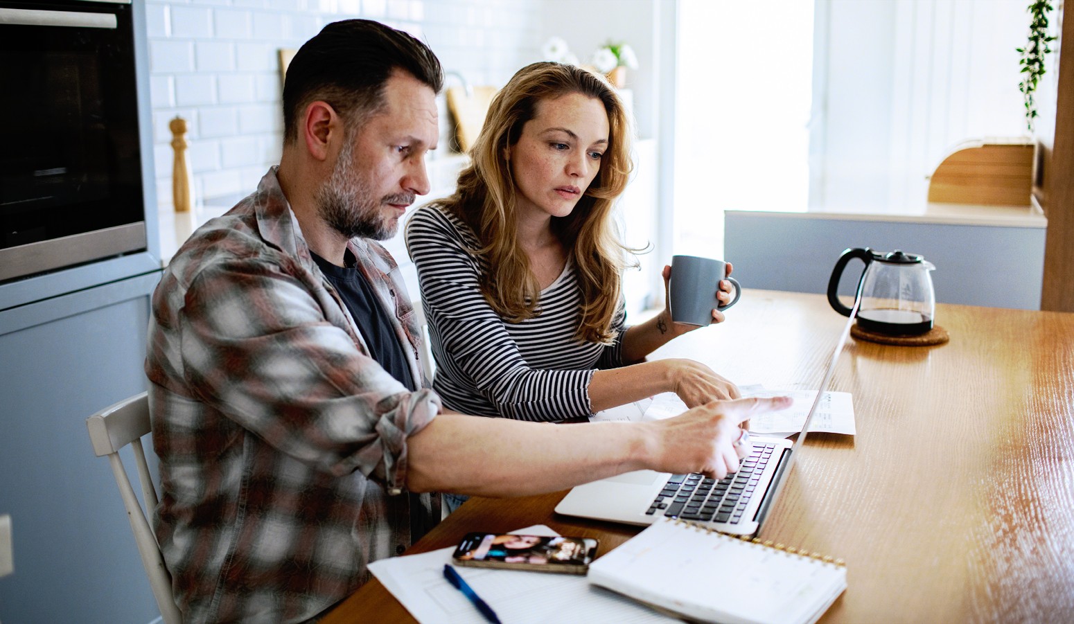 A man and a woman sitting at a table carefully looking at a laptop