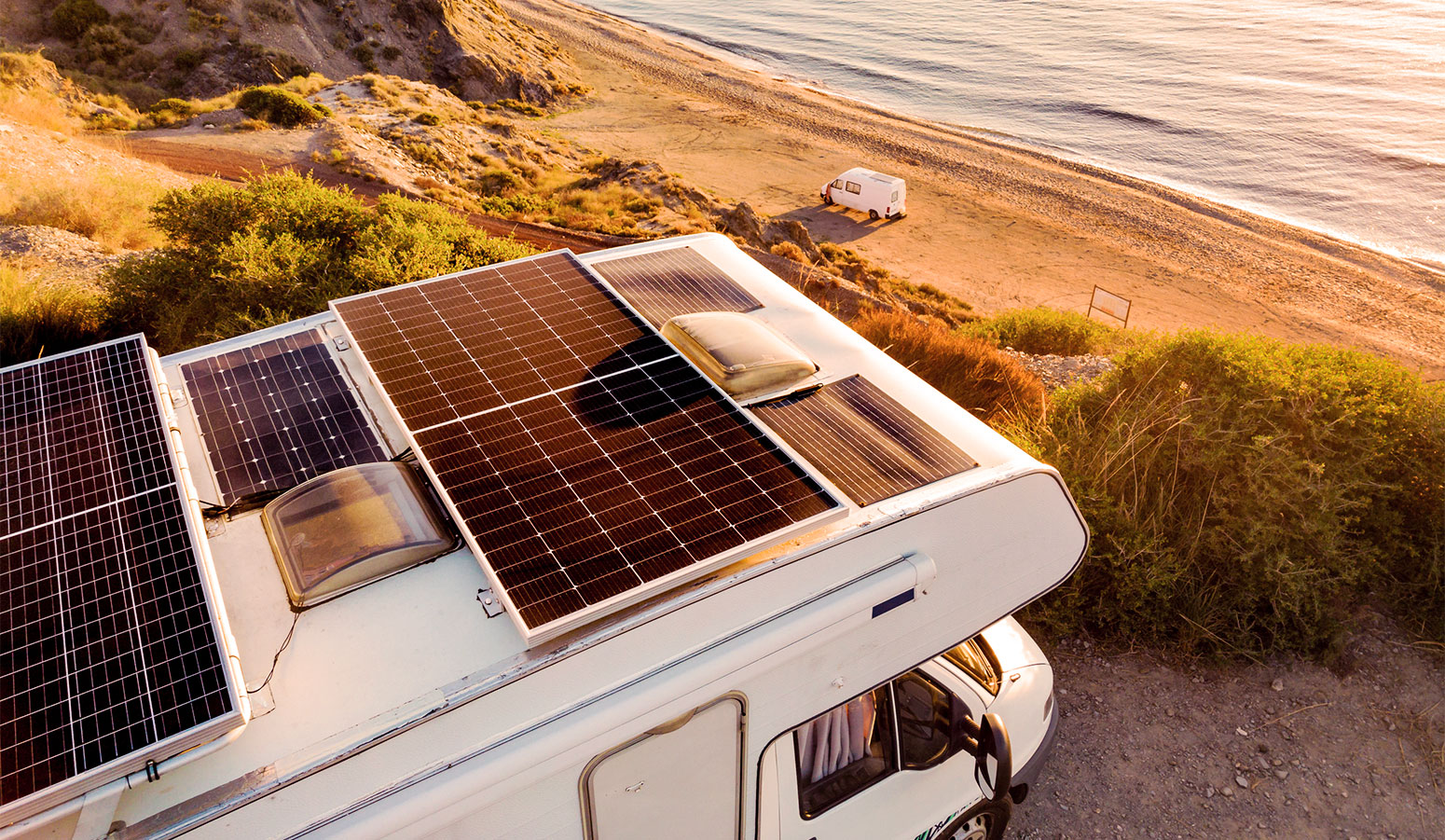 An RV parked by the ocean during golden hour with solar panels on its roof.