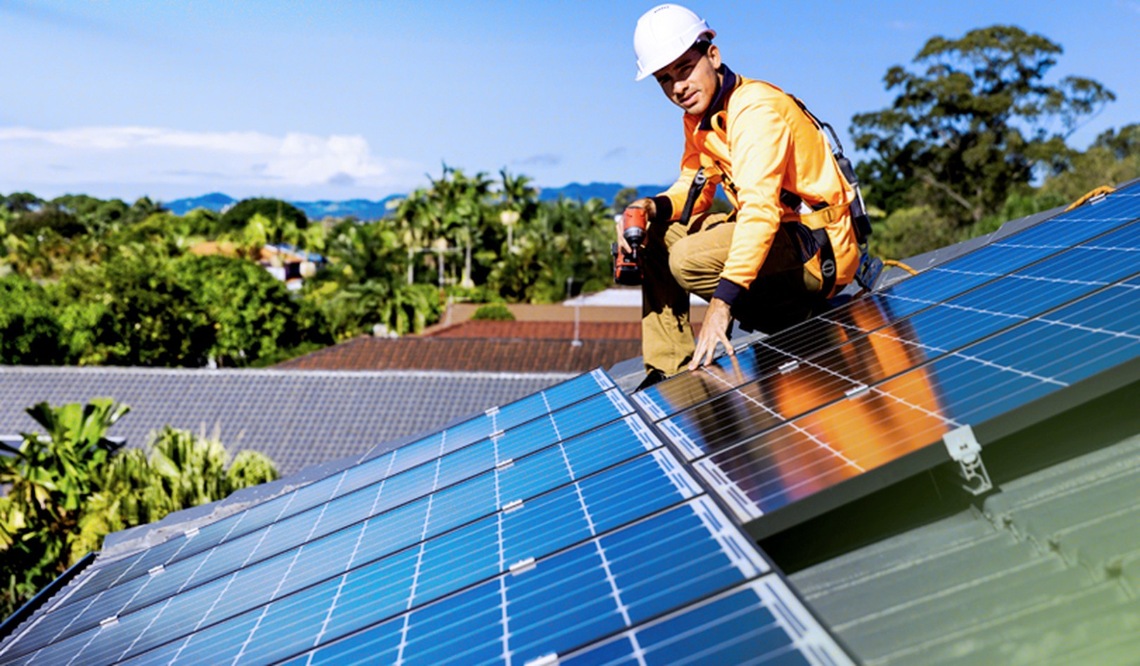 A photo of a man in work gear on a sunny roof installing solar panels