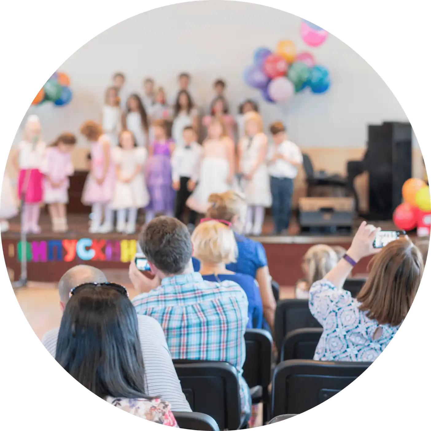 Children on stage during a school concert, parents in the audience filming them on their phones