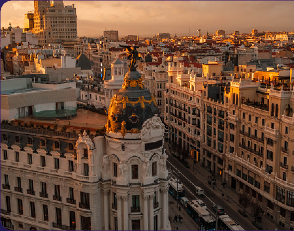 Aerial view of a cityscape at sunset, featuring a prominent ornate building with a dome and busy streets lined with historic architecture.