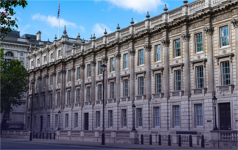 A grand, historic building with ornate architecture, numerous windows, and a flag on the roof, set against a blue sky with scattered clouds.