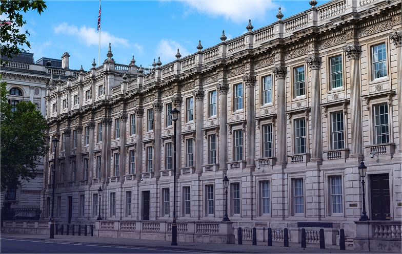 Historic building with ornate architecture, tall windows, and a flag on the roof, under a blue sky with clouds.