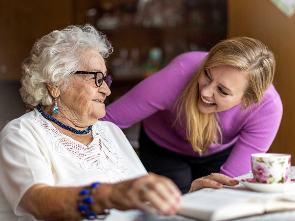 Older woman reading at table with younger woman