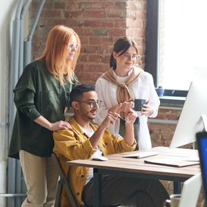 Group of three casually-dressed coworkers huddled around a computer monitor