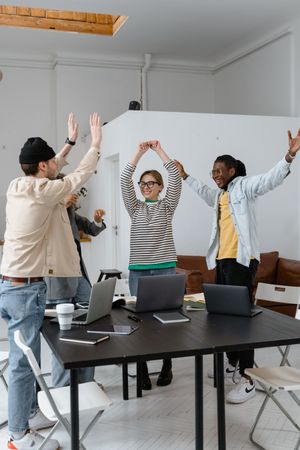 Diverse team of three people at a casual office with arms raised in celebration